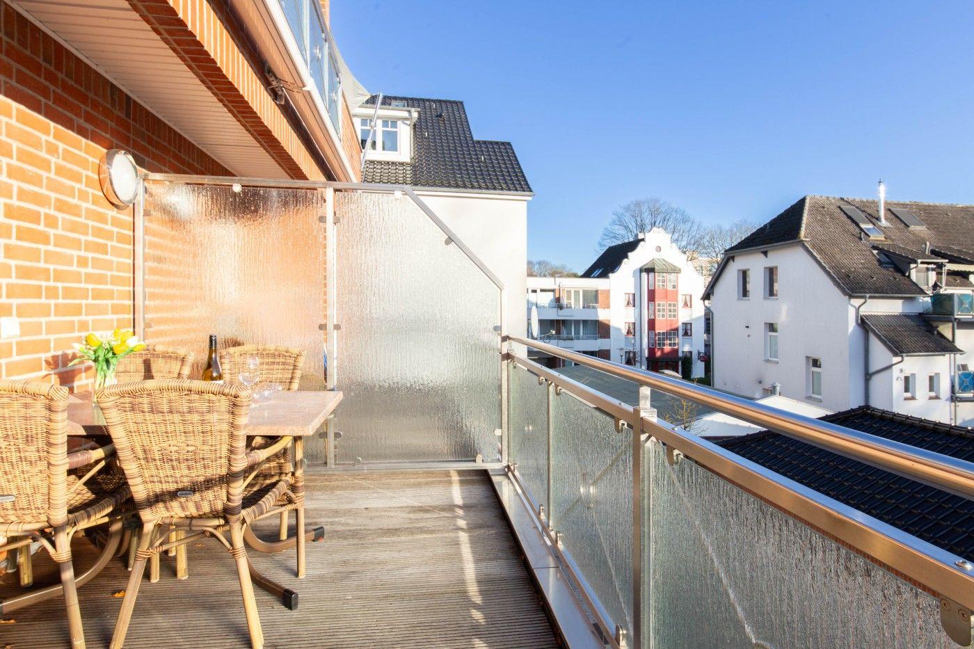Terrasse mit Tisch und Stühlen, Sicht auf Wohnhäuser und klaren Himmel.