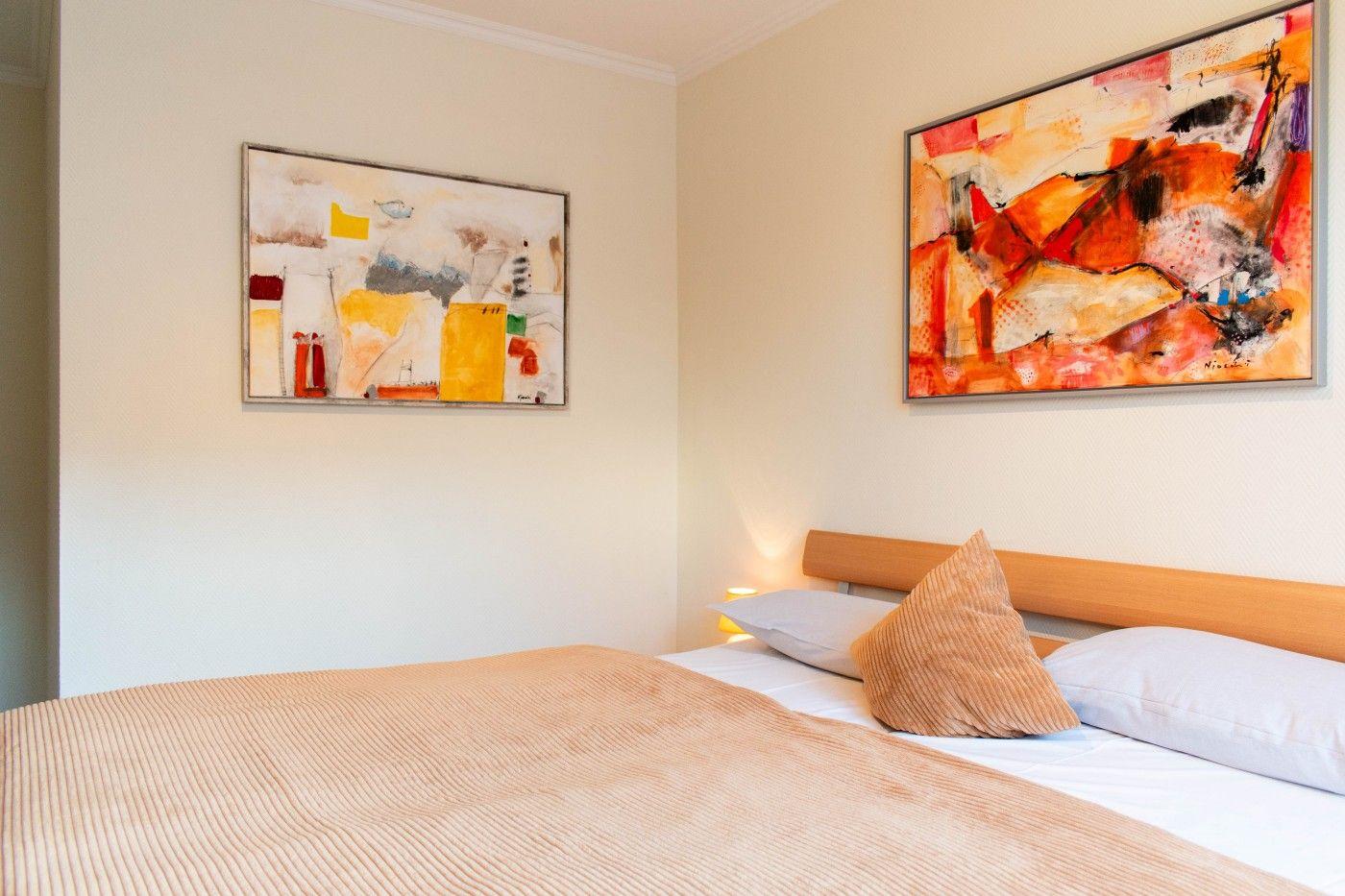 Schlafzimmer mit Bett, Kissen und zwei Wandbildern.