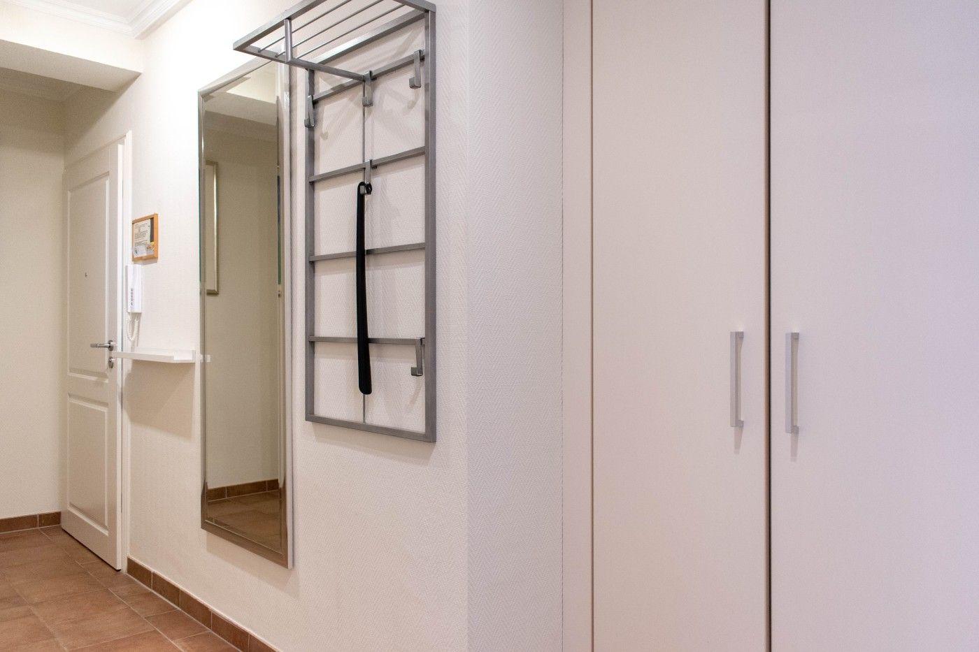 Flur mit Spiegel, Kleiderständer und Schrank. Tür und Bodenfliesen sichtbar.