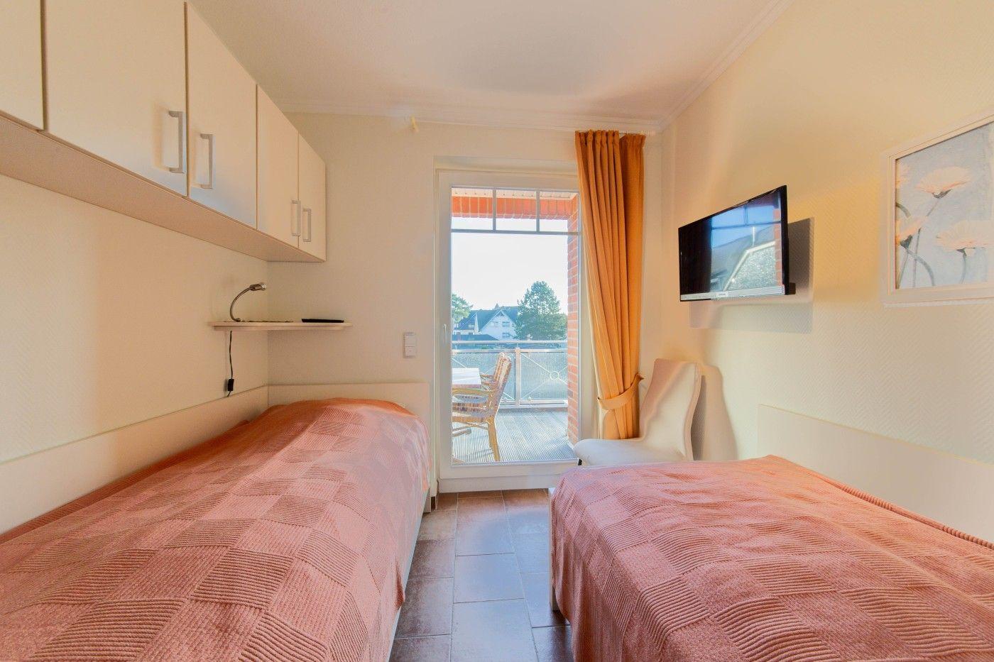 Zwei Betten, TV, Balkon mit Sitzgelegenheit und Küchenzeile im Zimmer.