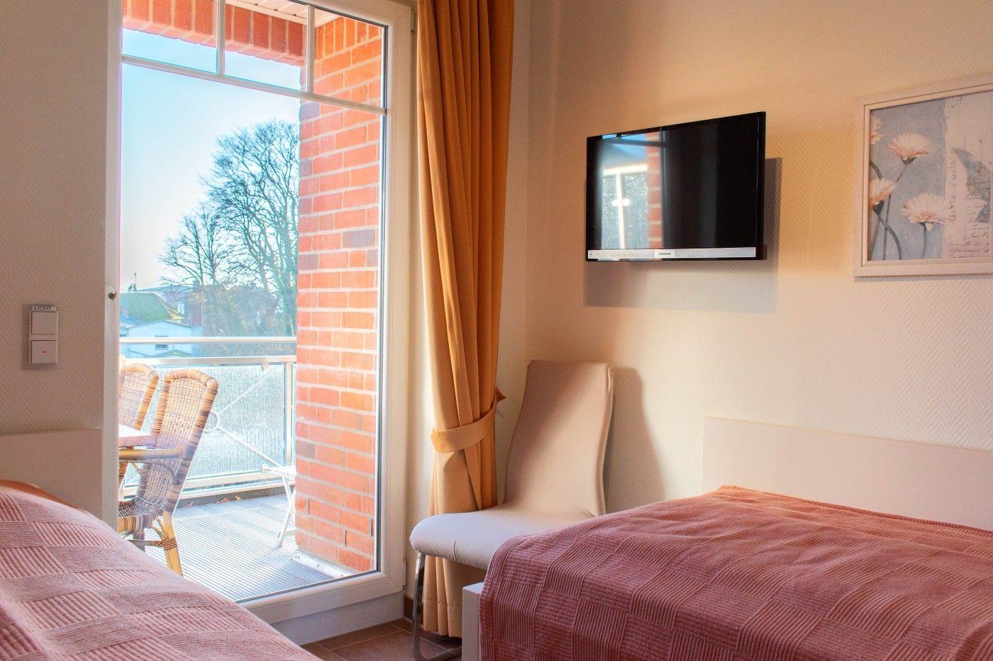 Zimmer mit Balkon, Bett, Fernseher und Wandbild.