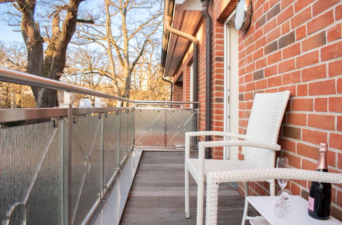 Terrasse mit weißem Stuhl, Tisch und Sektflasche an roter Ziegelwand.