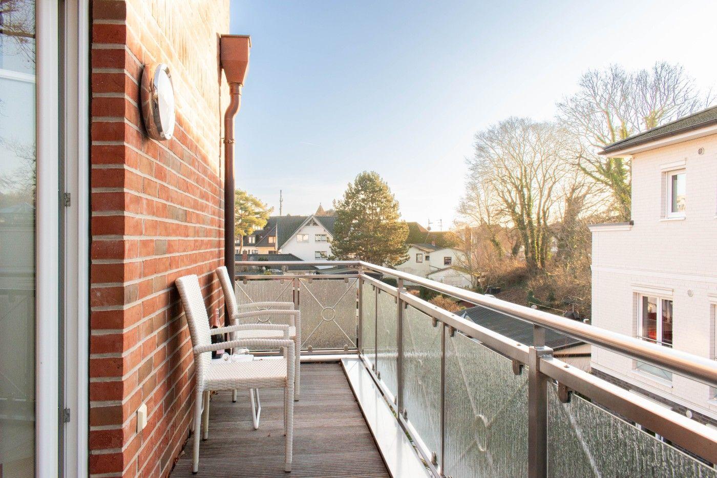 Terrasse mit zwei weißen Stühlen und Blick auf Wohnhäuser und Bäume.