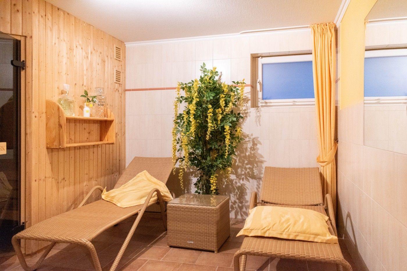 Sauna mit zwei Liegen, Pflanze und Fenster mit Vorhang.