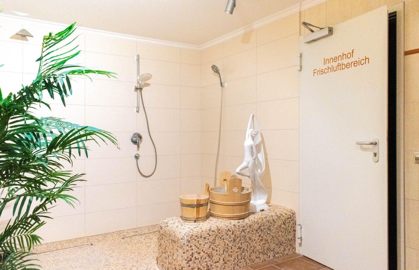 Dusche mit Pflanze, Holzwaschbecken und Statue. Tür zum Frischluftbereich.