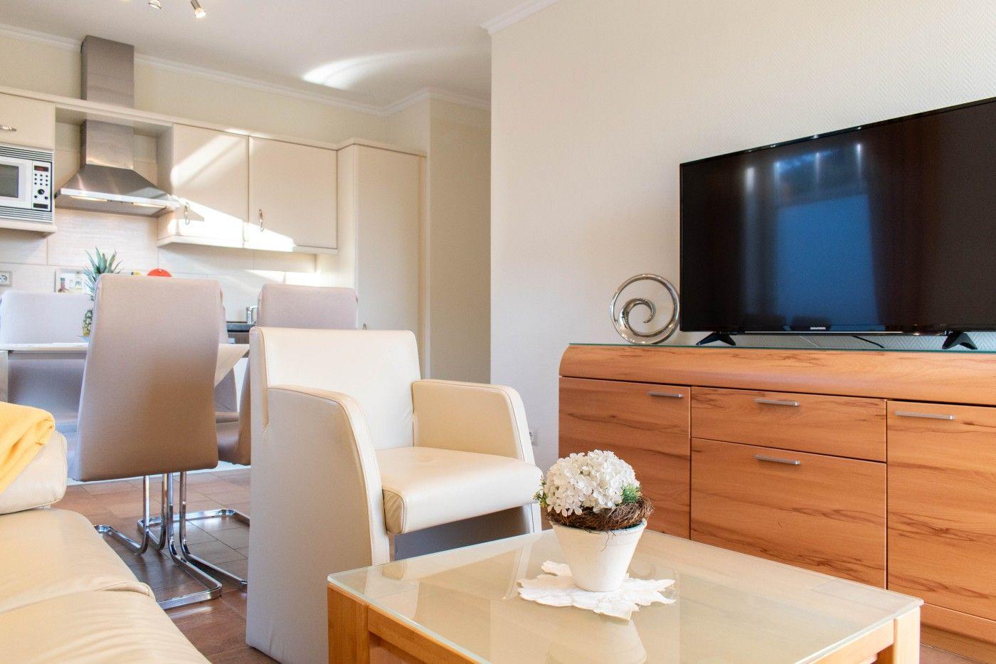 Wohnbereich mit TV, Couch und Küchenbereich im Hintergrund.