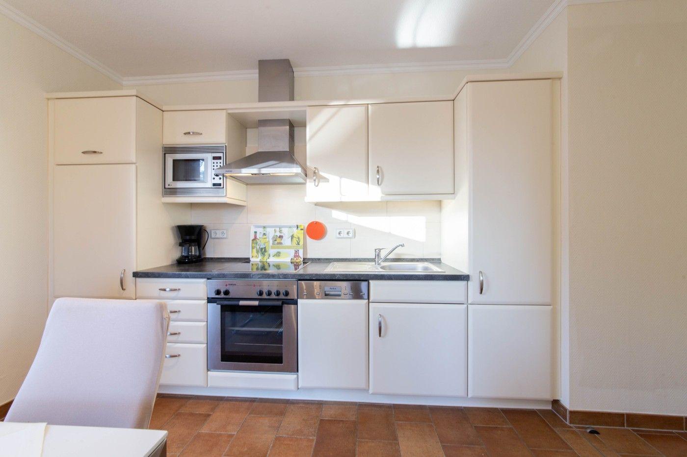 Küche mit weißen Schränken, Edelstahlspüle, Herd und Dunstabzugshaube.