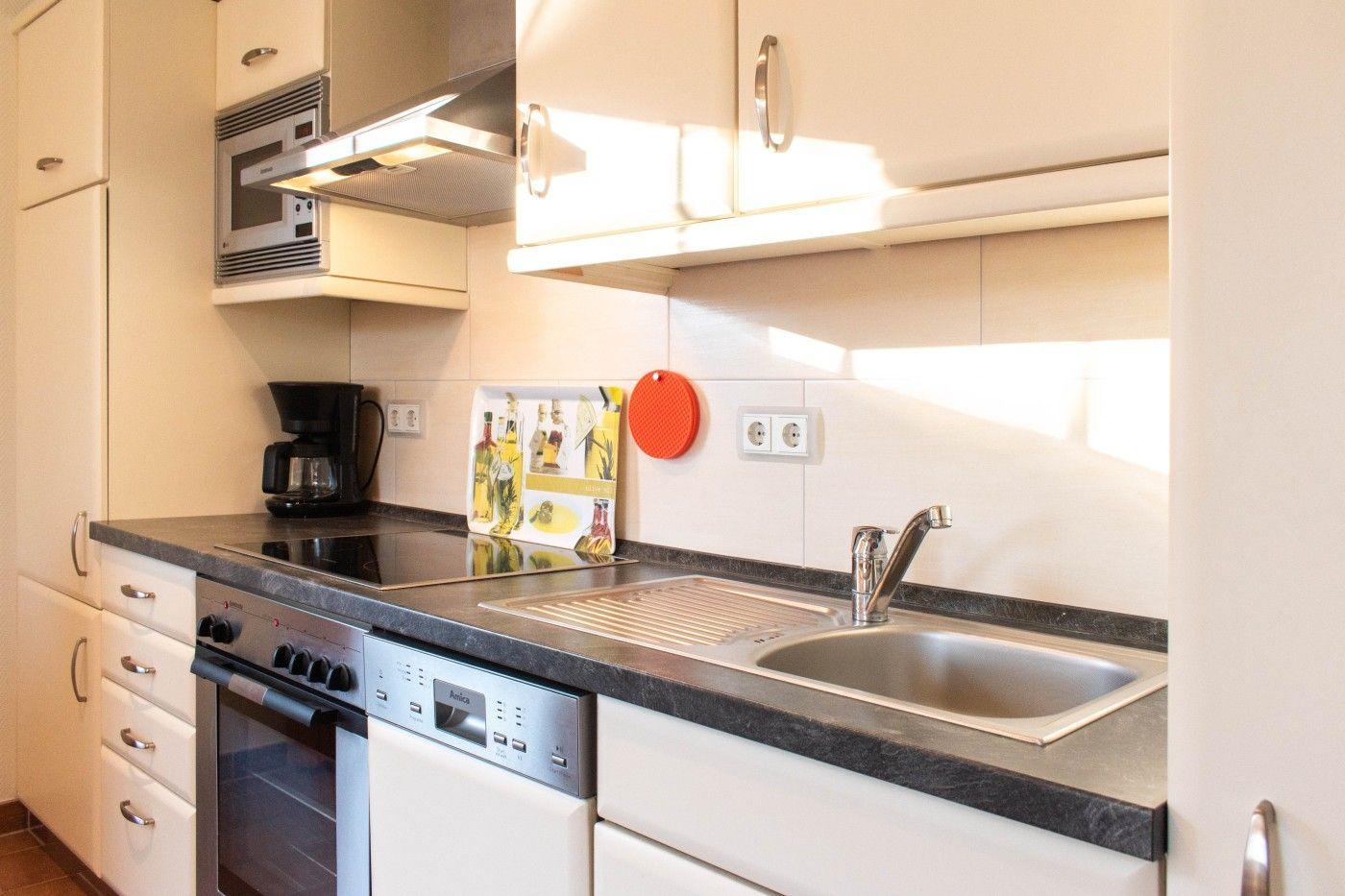 Küche mit Arbeitsplatte, Spüle, Kochfeld und integriertem Backofen.