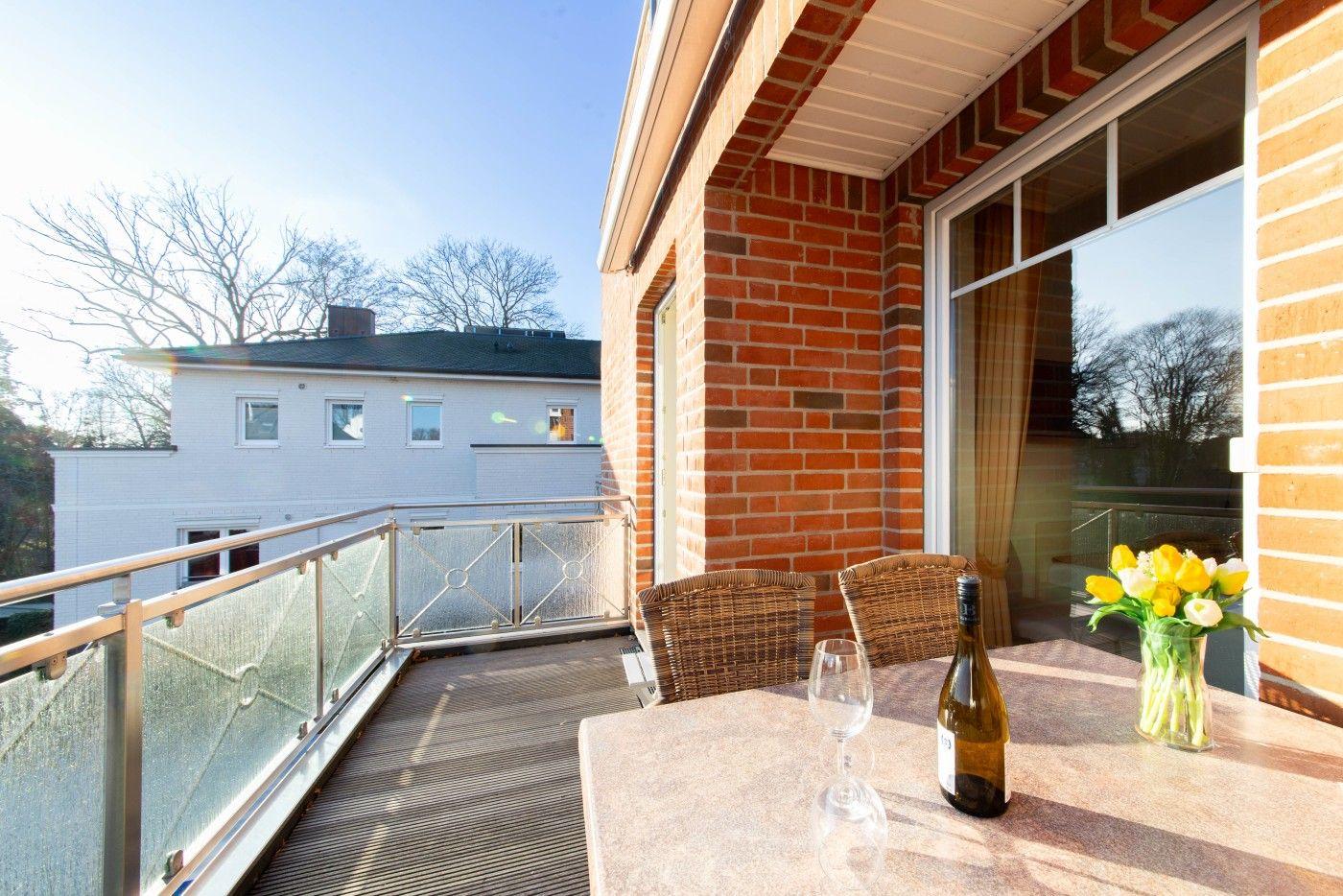 Terrasse mit Tisch, Stühlen, Wein und Blumen. Blick auf Haus und Bäume.
