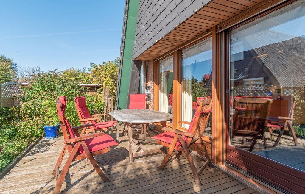 Terrasse mit Holztisch und roten Stühlen, angrenzend an ein Haus mit Glasfront.