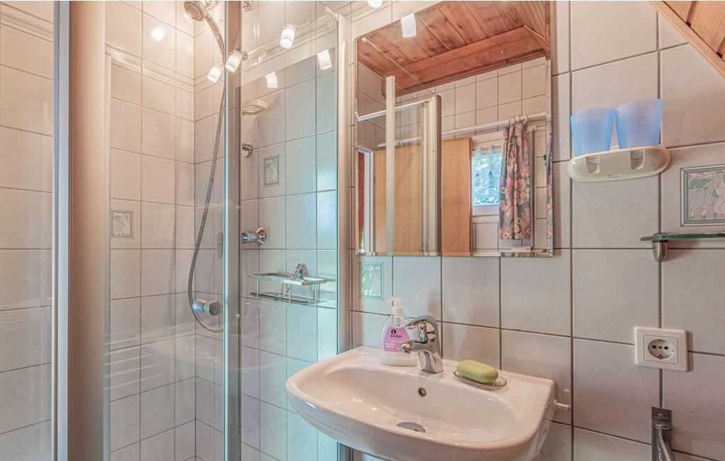 Badezimmer mit Dusche, Waschbecken und Spiegel. Holzdecke und Fliesenwand.