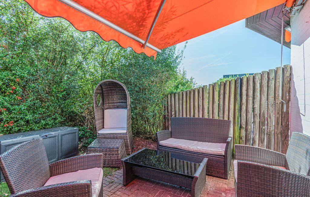 Terrasse mit Sitzgruppe unter orangefarbenem Sonnenschutz, umgeben von Grün und Holzzaun.