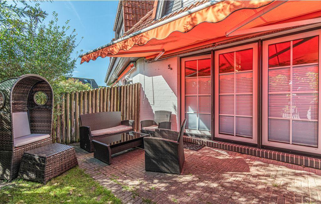 Terrasse mit Rattanmöbeln und orangefarbenem Markisenüberdachung. Hinterhof mit Holzzaun und Grünfläche.