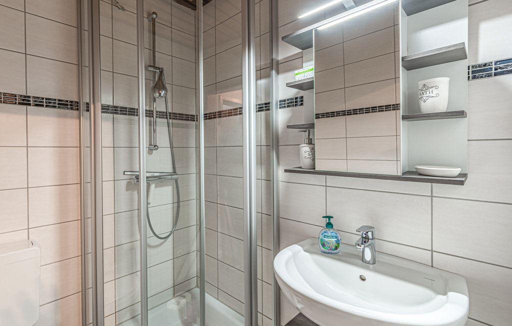 Duschkabine mit Glaswand, Waschbecken und Spiegelschrank mit Ablageflächen.