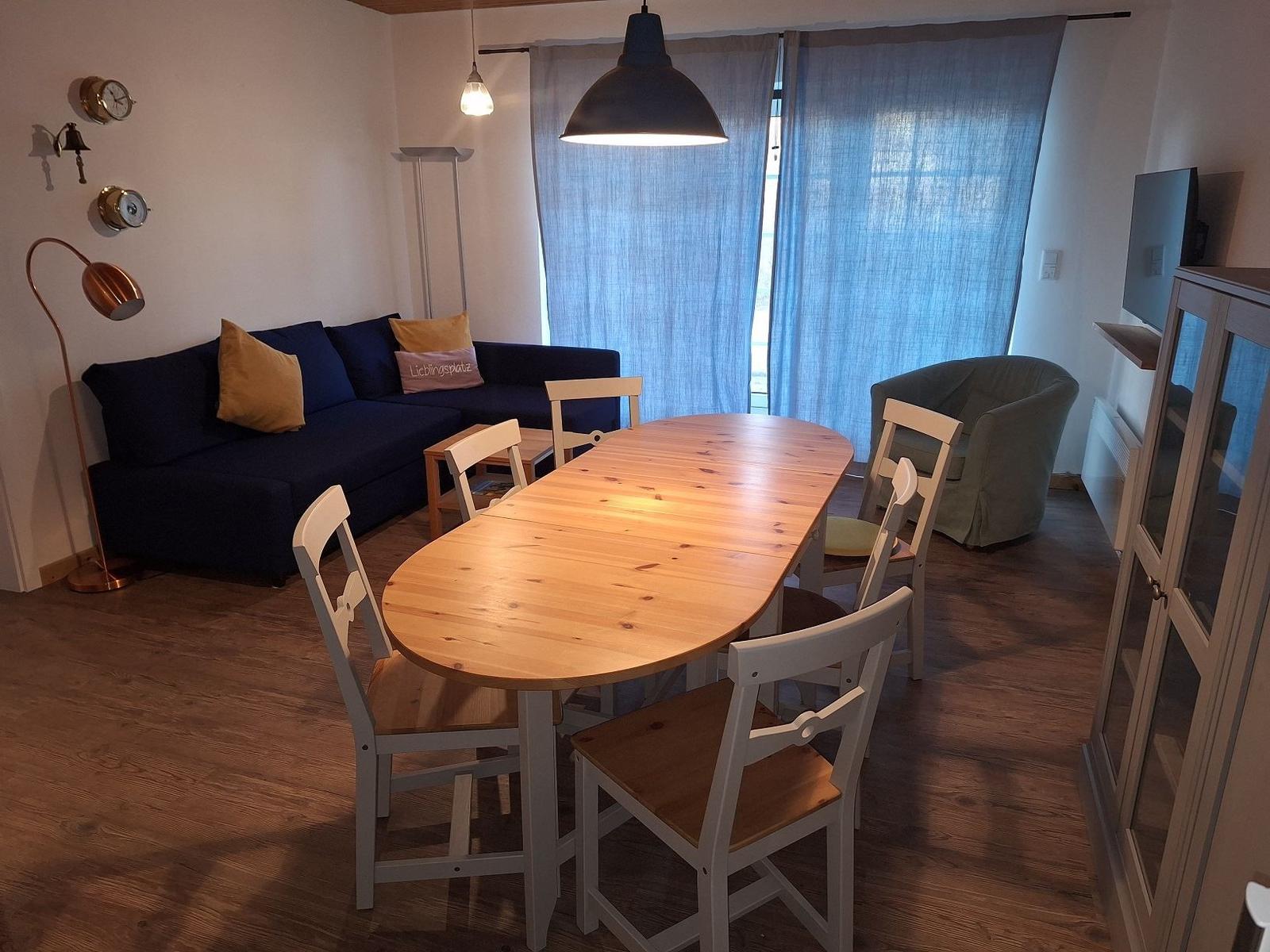 Esszimmer mit Holztisch, Stühlen und Sofa. Fenster mit blauen Vorhängen.