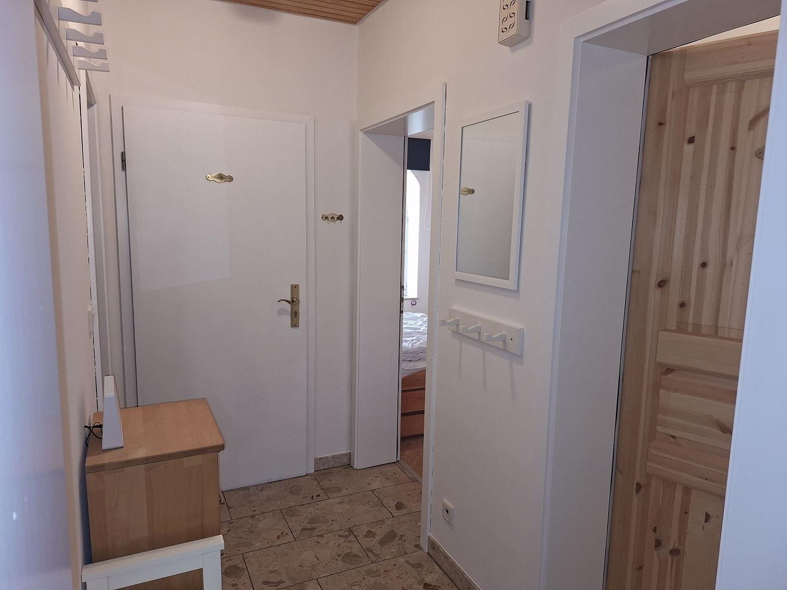Eingangsbereich mit Holztür, Spiegel und Kleiderhaken. Durchgang zu Schlafzimmer und Holzschrank.