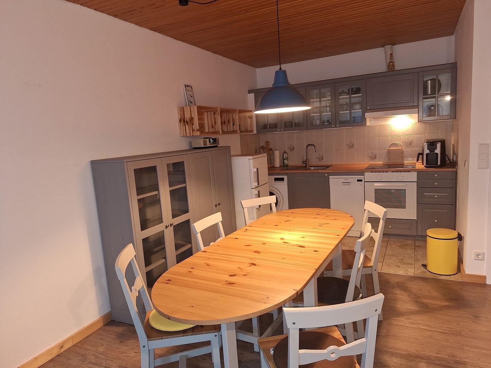 Küche mit Essbereich, Holztisch, weißen Stühlen und grauen Schränken.