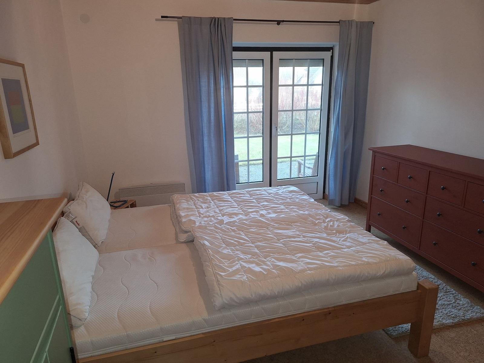 Schlafzimmer mit Bett, Schrank und Fenster zur Außenterrasse.