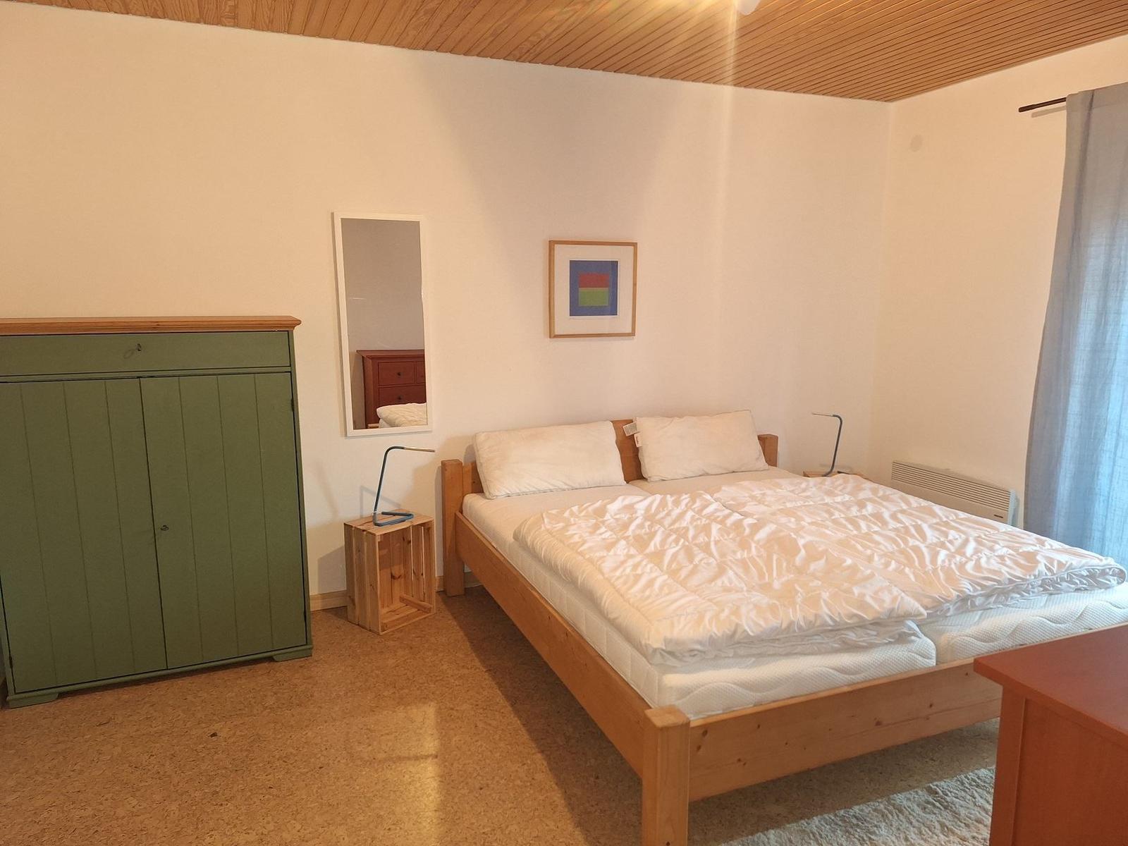 Schlafzimmer mit Holzbett, grünem Schrank und Spiegel an der Wand.