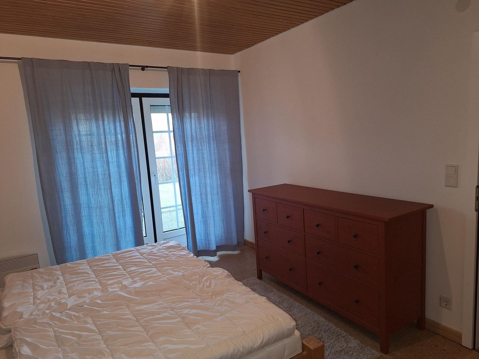 Schlafzimmer mit Bett, Schrank und Fenster mit Vorhängen.