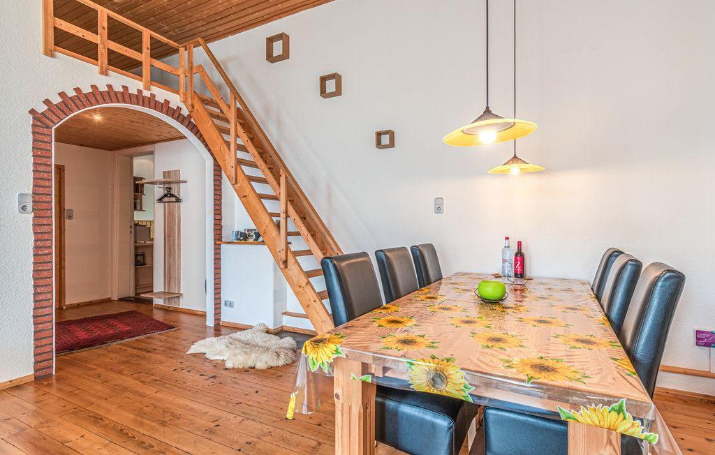 Esszimmer mit Tisch, Stühlen und Holztreppe zur oberen Etage.