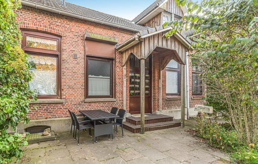 Rotes Backsteinhaus mit Holzveranda und Außentisch. Umgeben von Grünflächen.