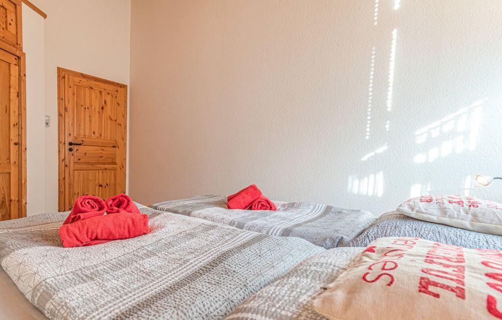 Zwei Betten mit gemusterten Bettwäsche und roten Handtüchern. Holztür und Wand sichtbar.