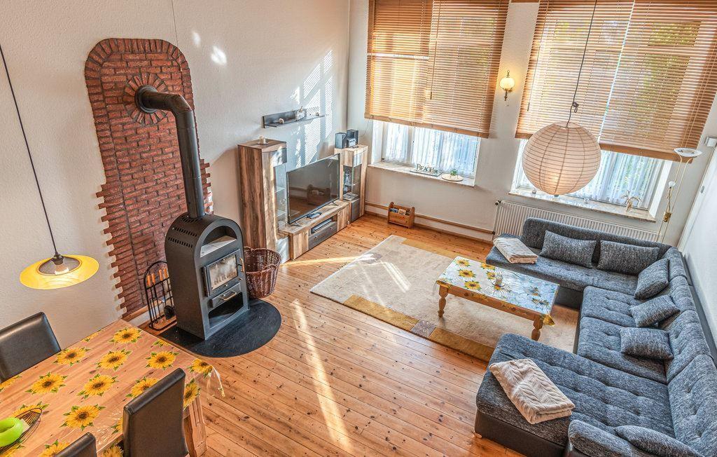 Wohnzimmer mit Sofa, Kamin und Holzboden. Fenster mit Jalousien und Esstisch mit Sonnenblumenmuster.