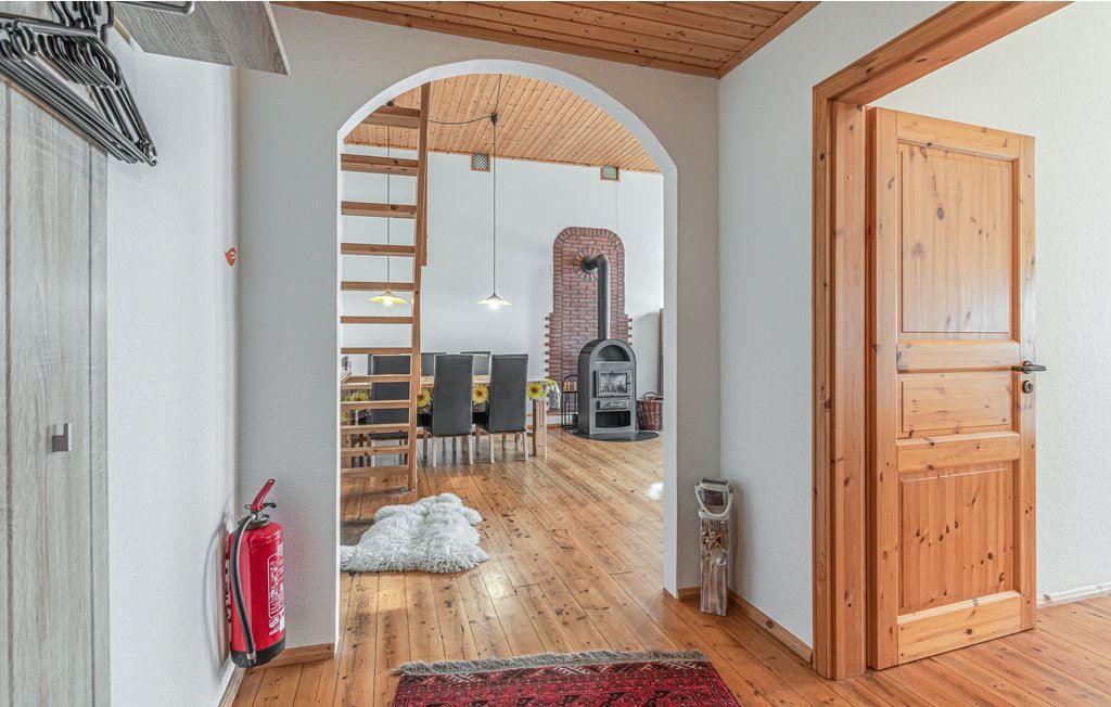 Haus mit Holzdecke, Tür und Sicht auf Esszimmer mit Holzboden und Kaminofen.