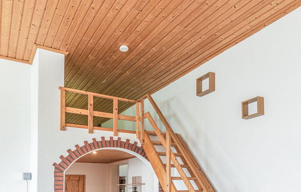 Holzgetäfelte Decke, Treppe zu einer Galerie mit Holzgeländer und zwei Wandregalen.