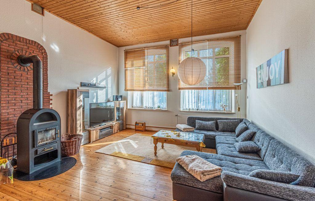 Wohnzimmer mit Holzboden, Sofa, Kamin und Fenstern mit Jalousien.