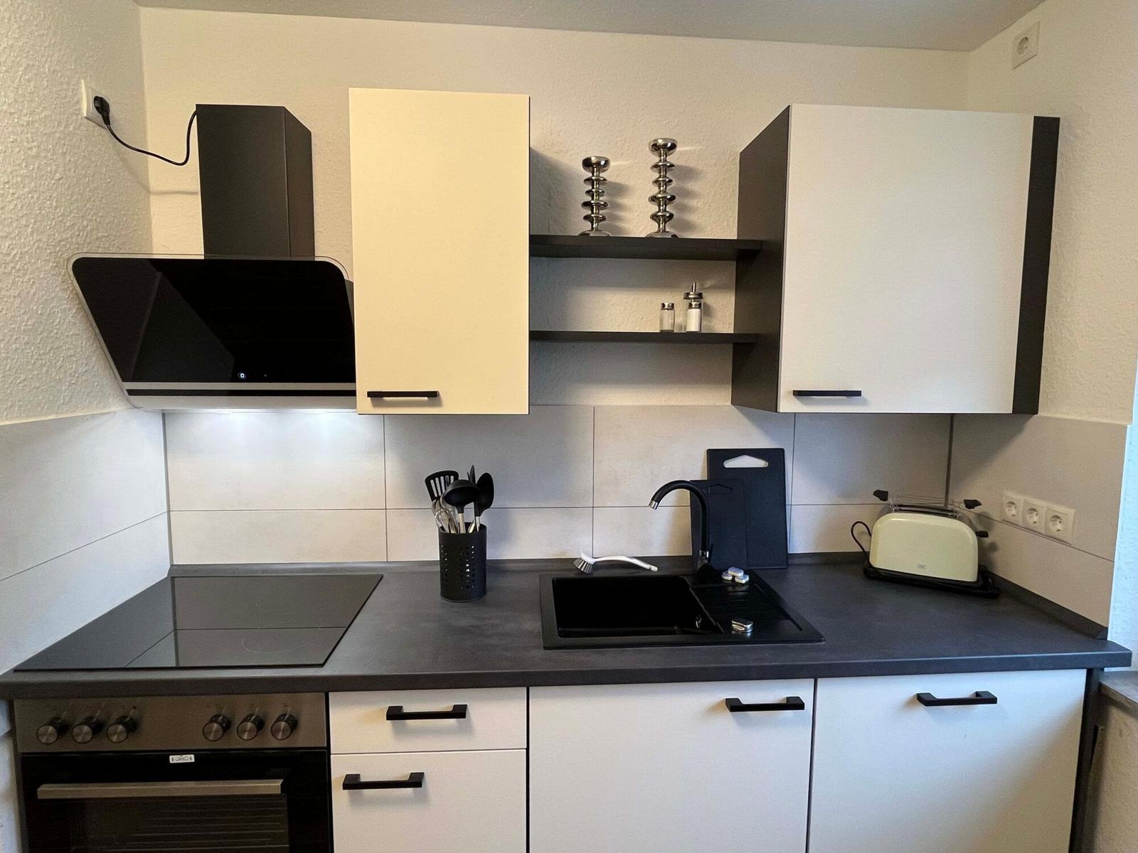 Küche mit Dunstabzug, Herd, Spüle und weißen Schränken.