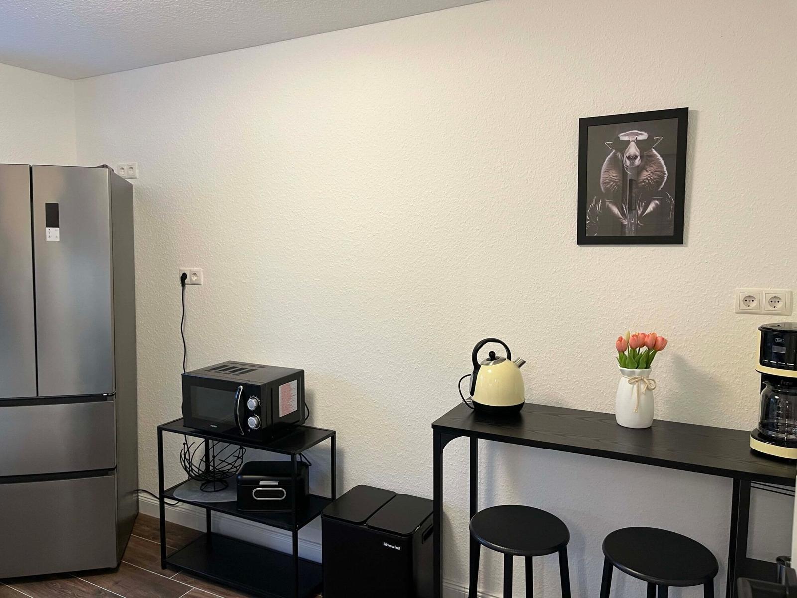 Küchenbereich mit Kühlschrank, Mikrowelle, Kaffeemaschine und Kanne auf Tisch mit Stühlen.