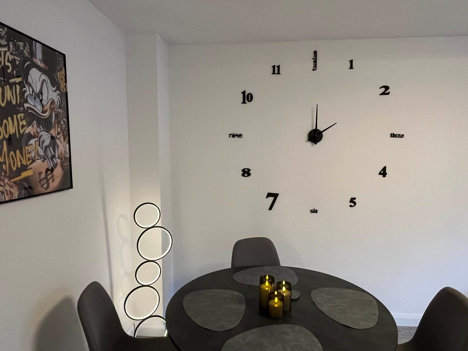 Esszimmer mit runder Tisch, Kerzen und Wanduhr mit Ziffern.