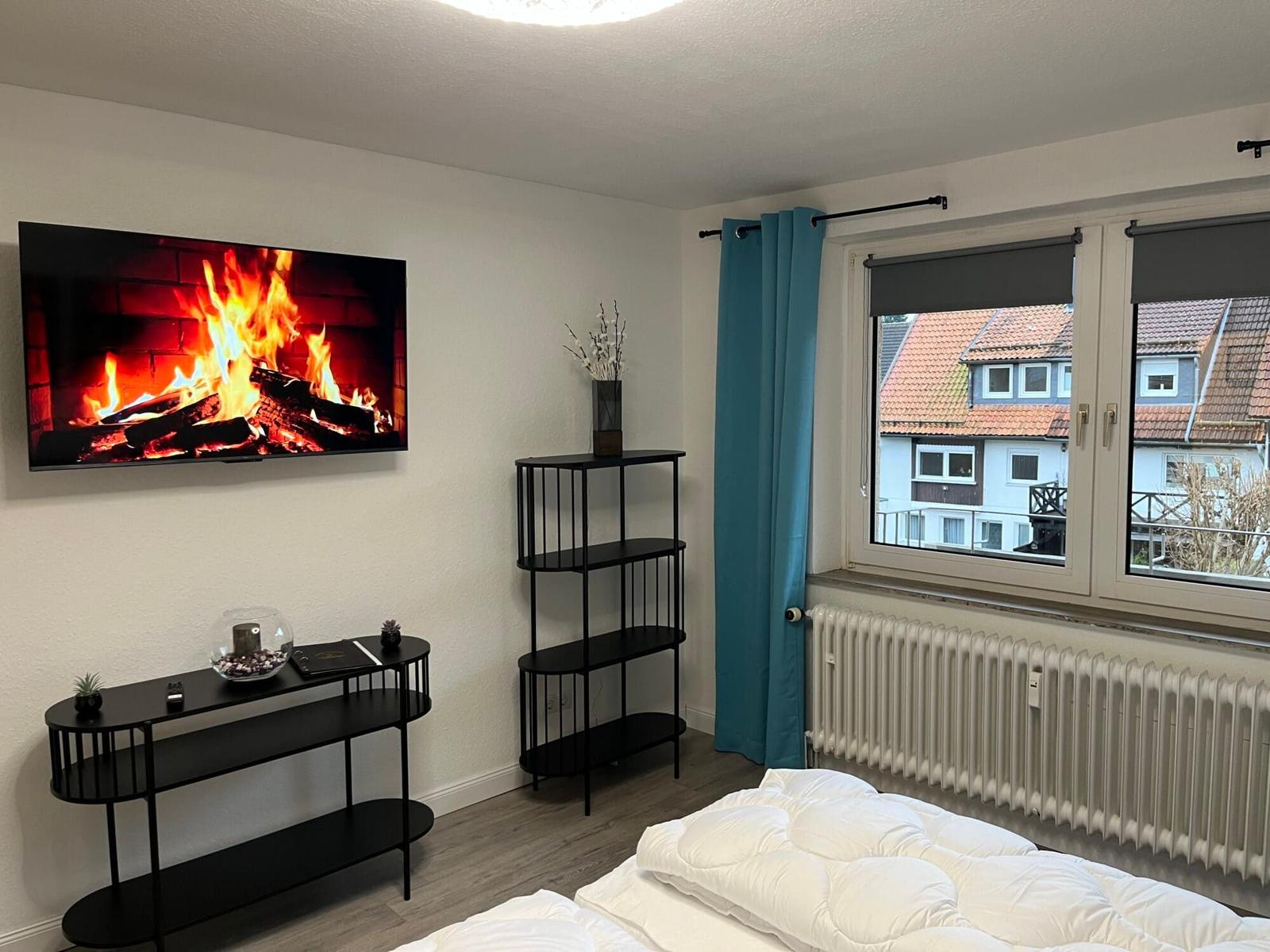 Zimmer mit Bett, Fernseher und Fenster mit Blick auf Dächer.