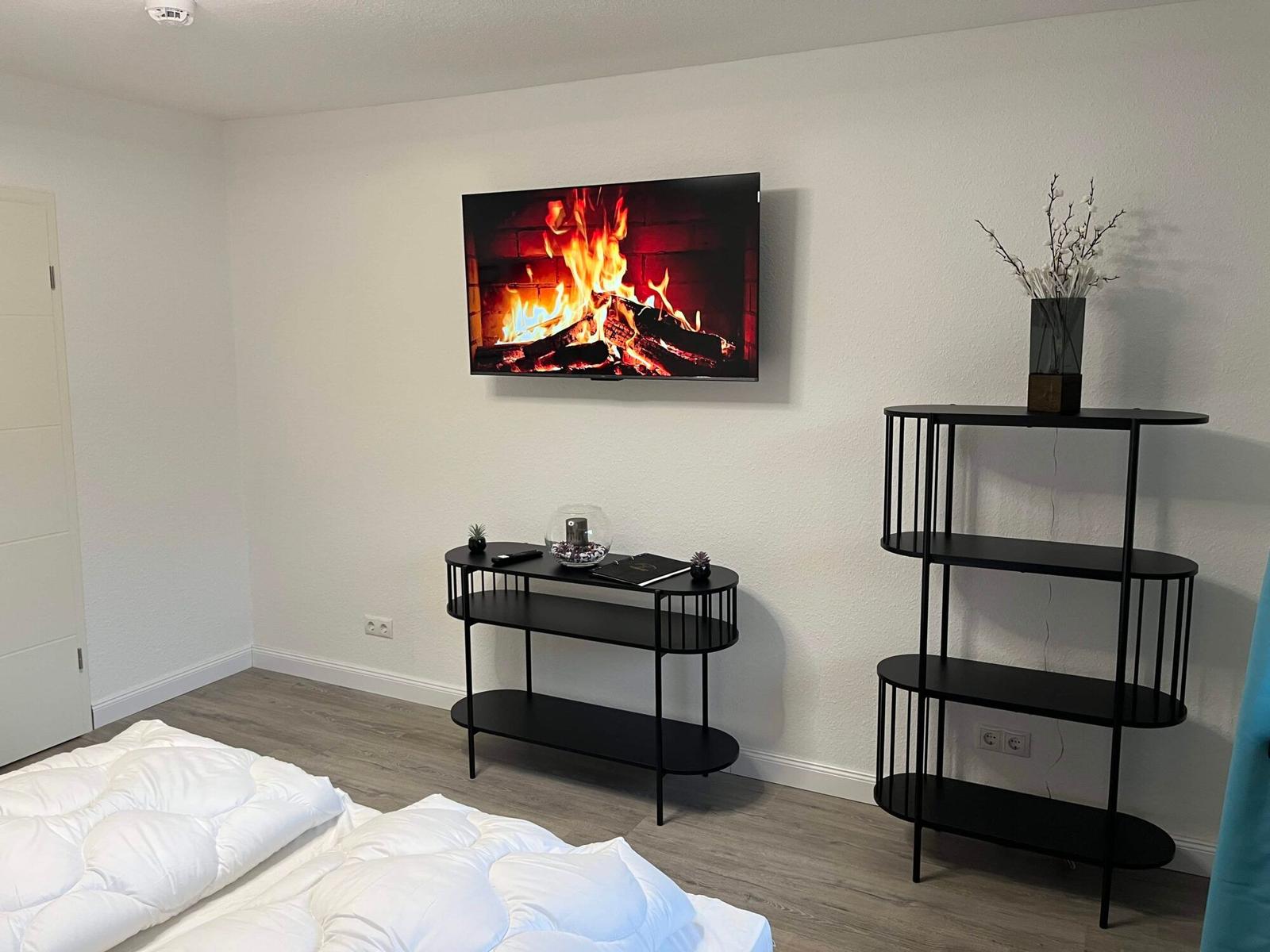 Schlafzimmer mit Bett, Fernseher und schwarzen Regalen.