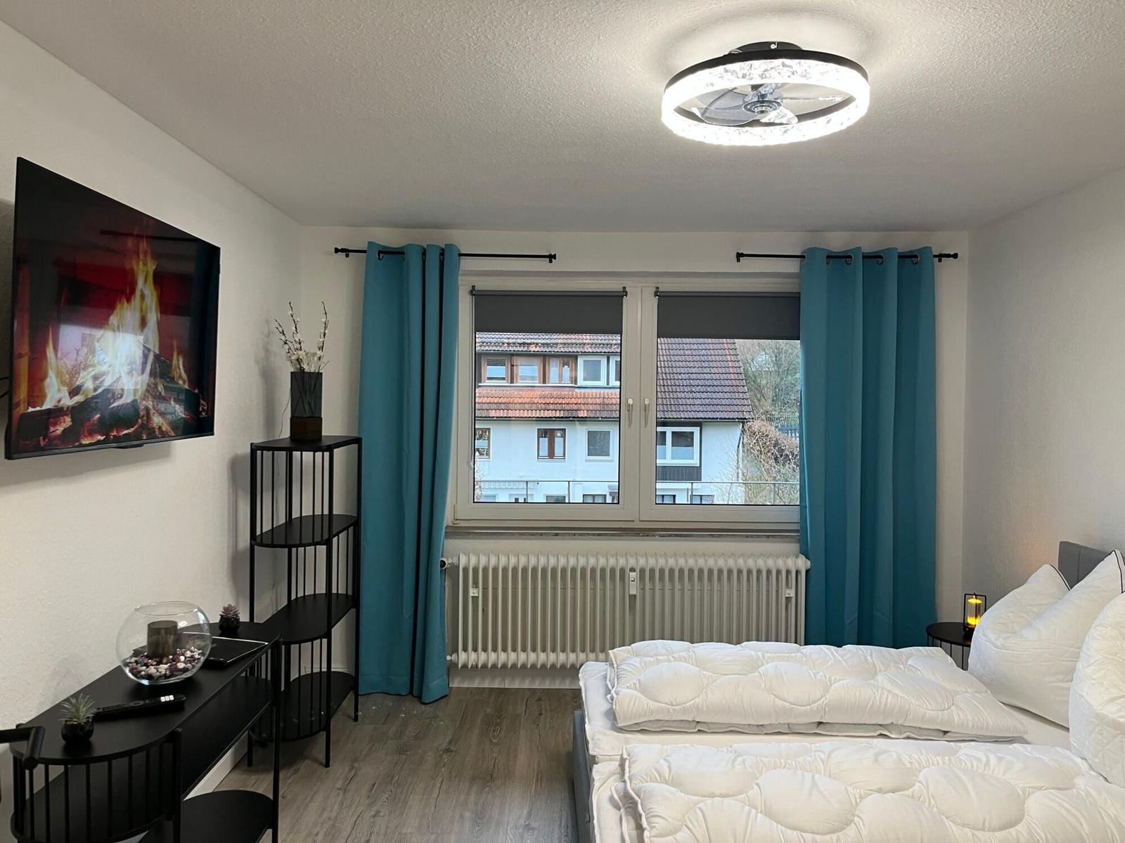 Schlafzimmer mit Bett, TV und Fenster mit Blick auf Gebäude.