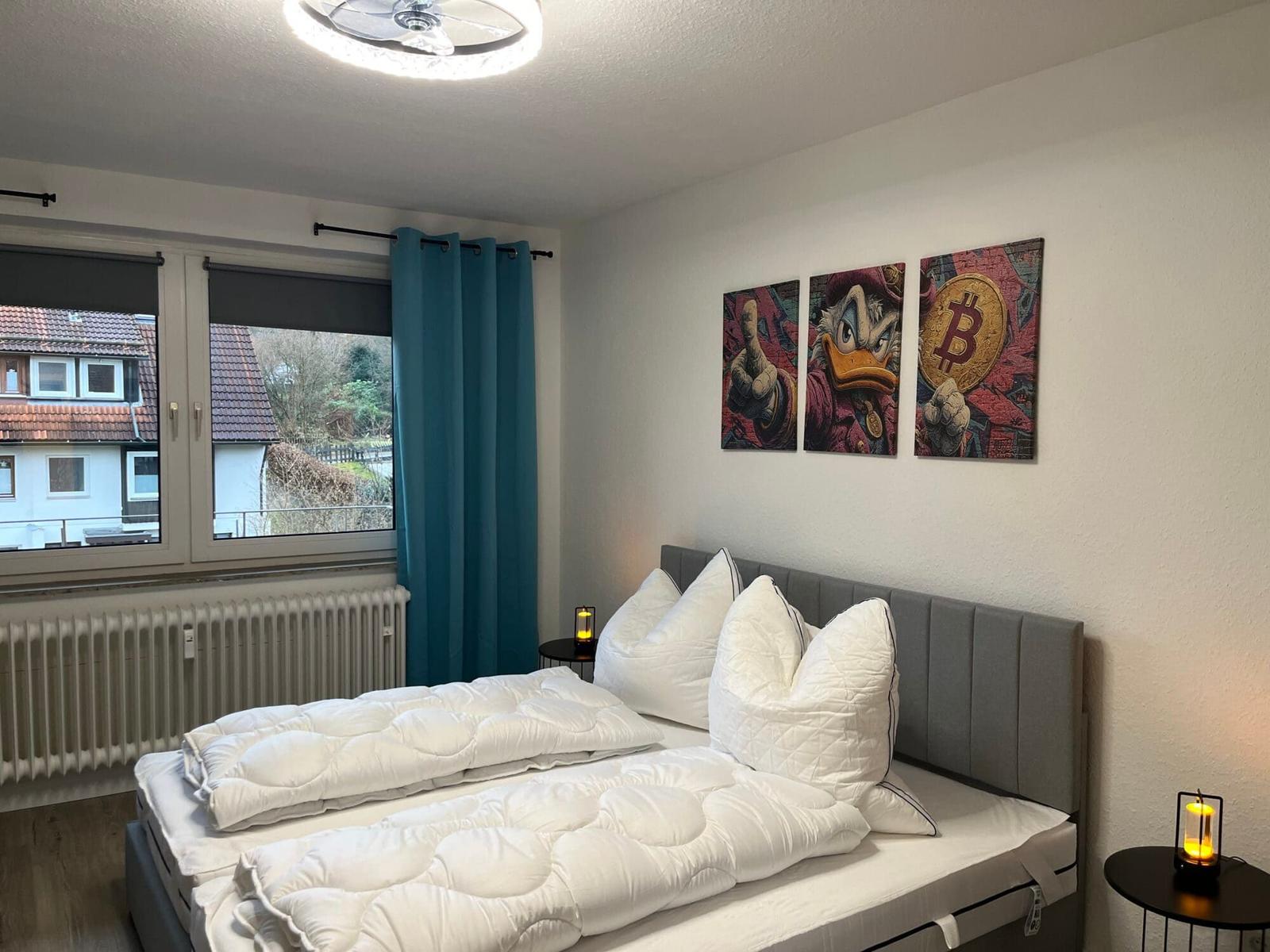 Schlafzimmer mit Bett, Fenster und Wandbildern.