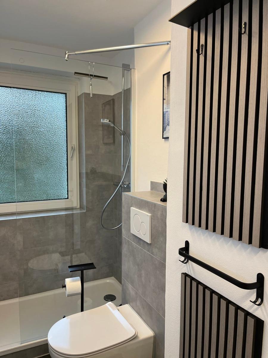 Badezimmer mit Dusche, Toilette und Fenster mit getöntem Glas.