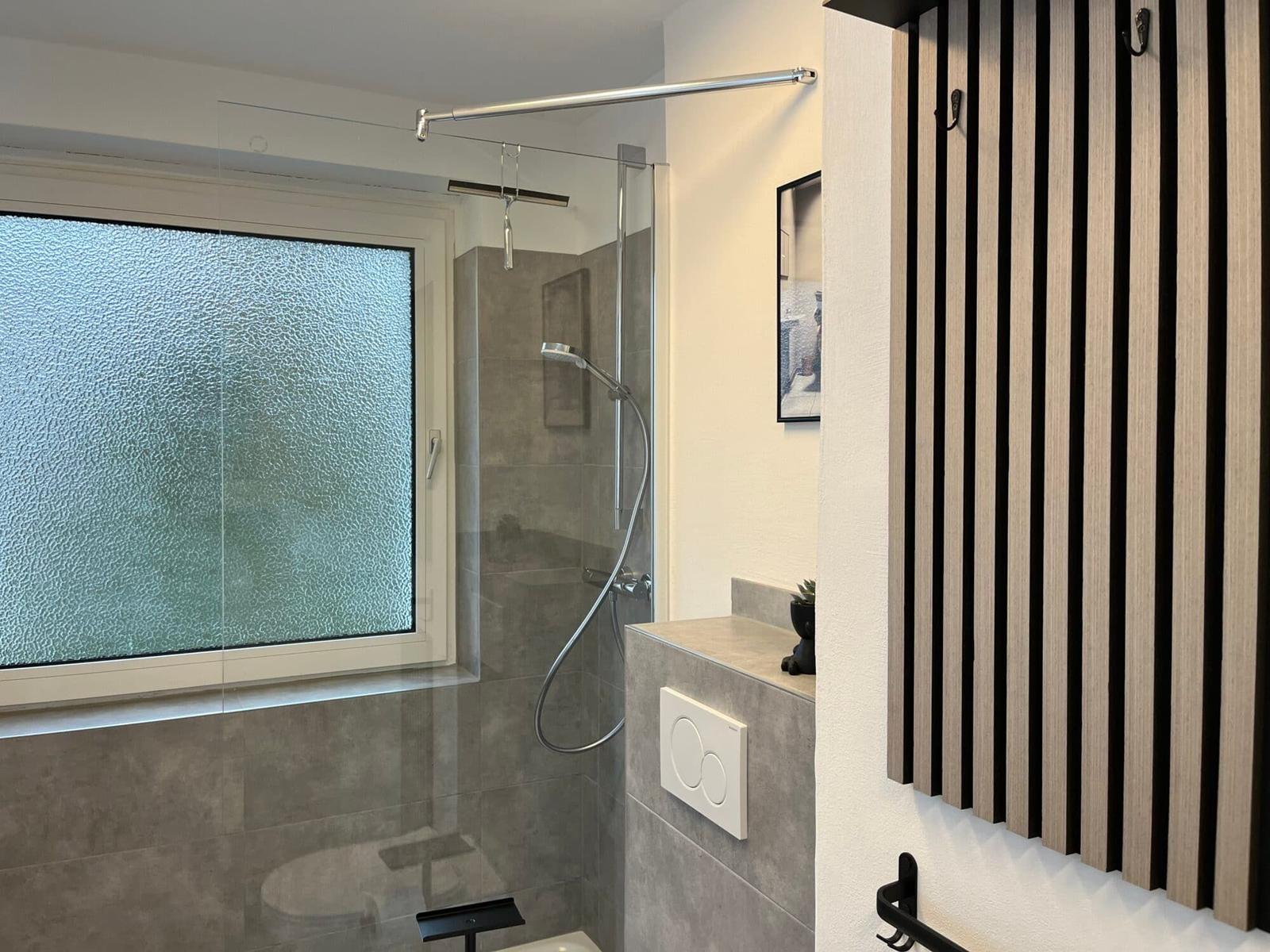 Badezimmer mit Dusche, Fenster und Holzpaneelen an der Wand.