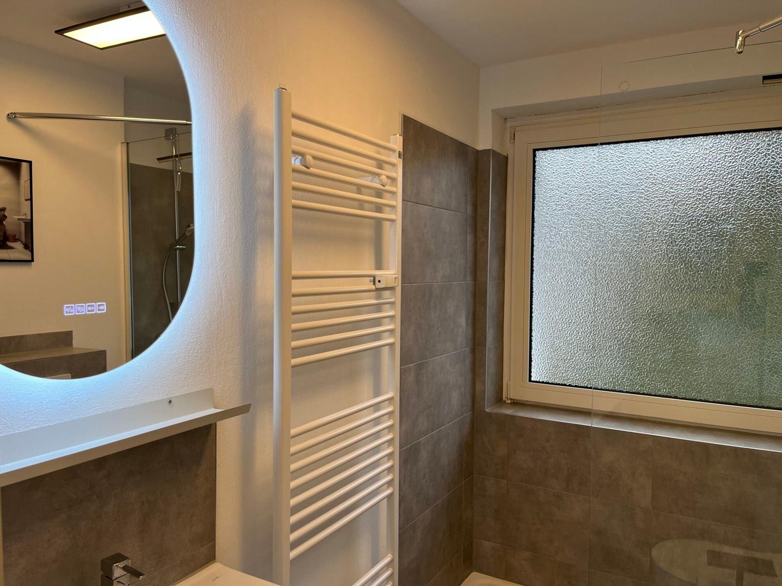 Badezimmer mit Dusche, Heizkörper und gefliestem Fensterbereich.