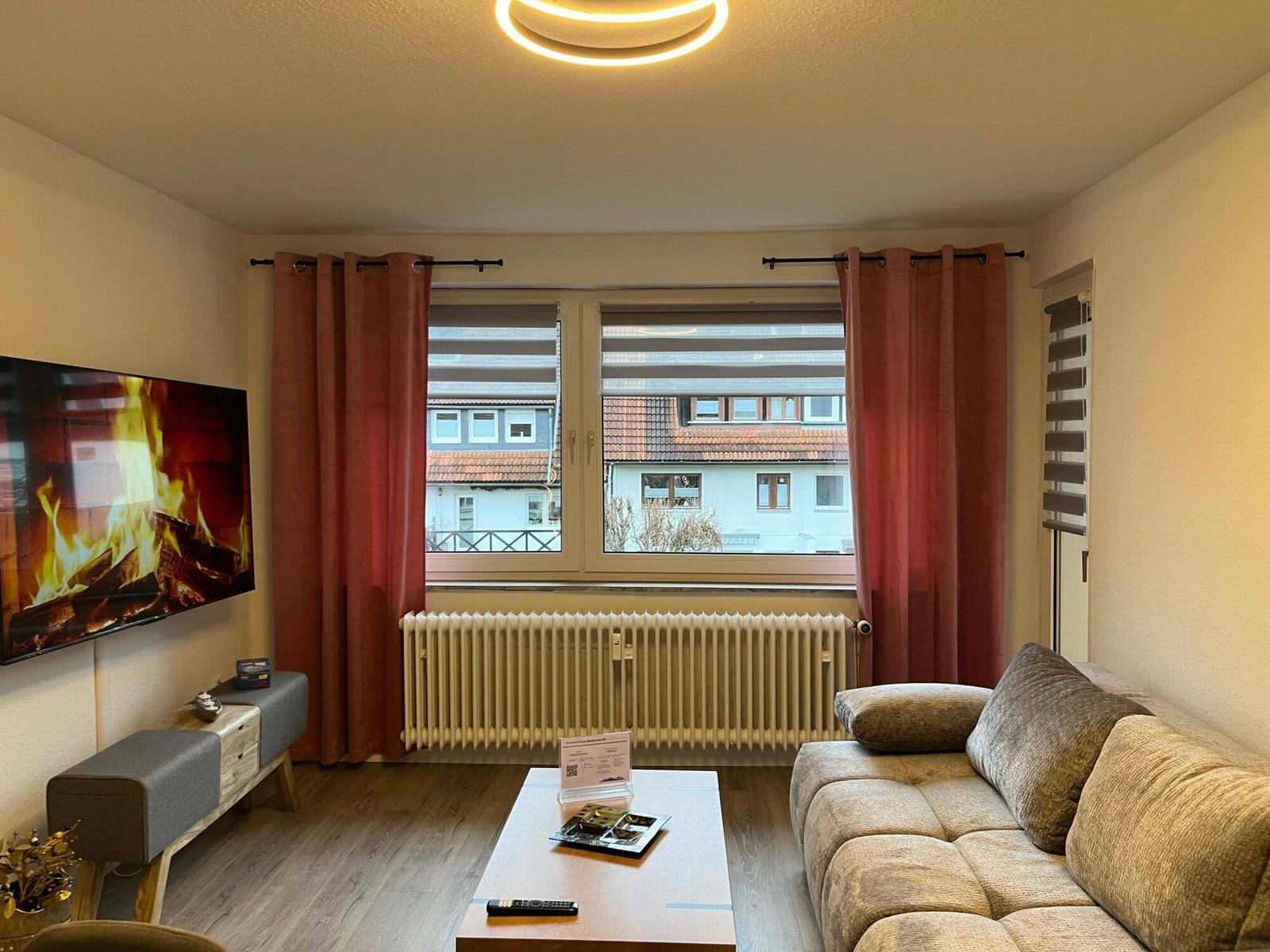 Wohnzimmer mit Sofa, Fernseher und Fenster mit Blick auf Gebäude