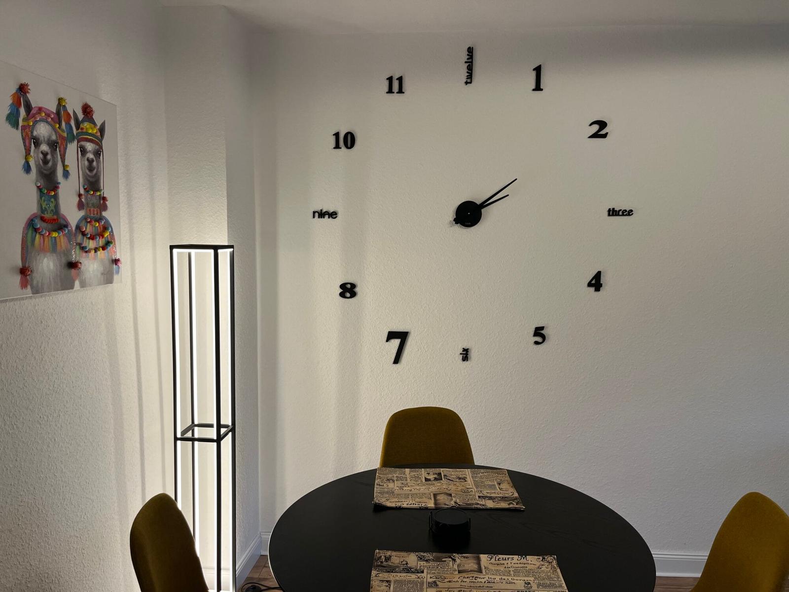 Esszimmer mit runder Tisch, gelben Stühlen und Wanduhr mit Ziffern.