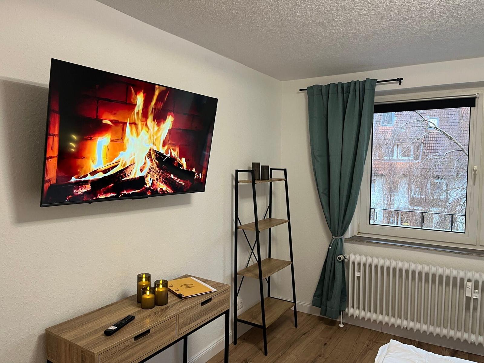 Wohnzimmer mit Fernseher, Schrank und Fenster mit Vorhang.