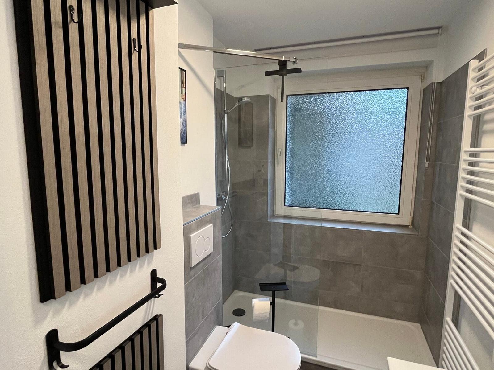 Badezimmer mit Dusche, Fenster und Toilette. Holz- und Metallgestaltung.