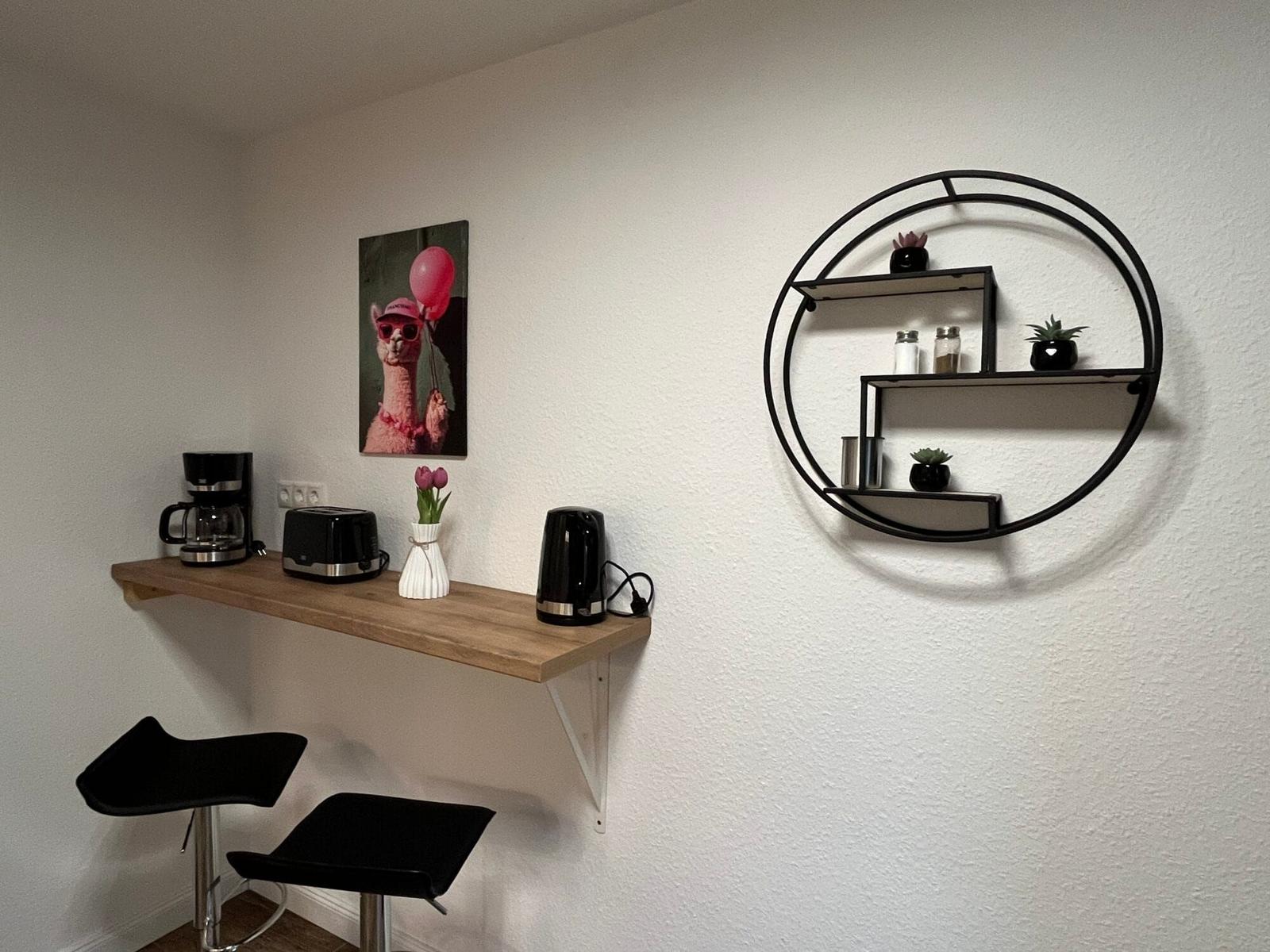 Küchenzeile mit Kaffeemaschine, Toaster und Wasserkocher. Wandregal mit Pflanzen und Gewürzen.