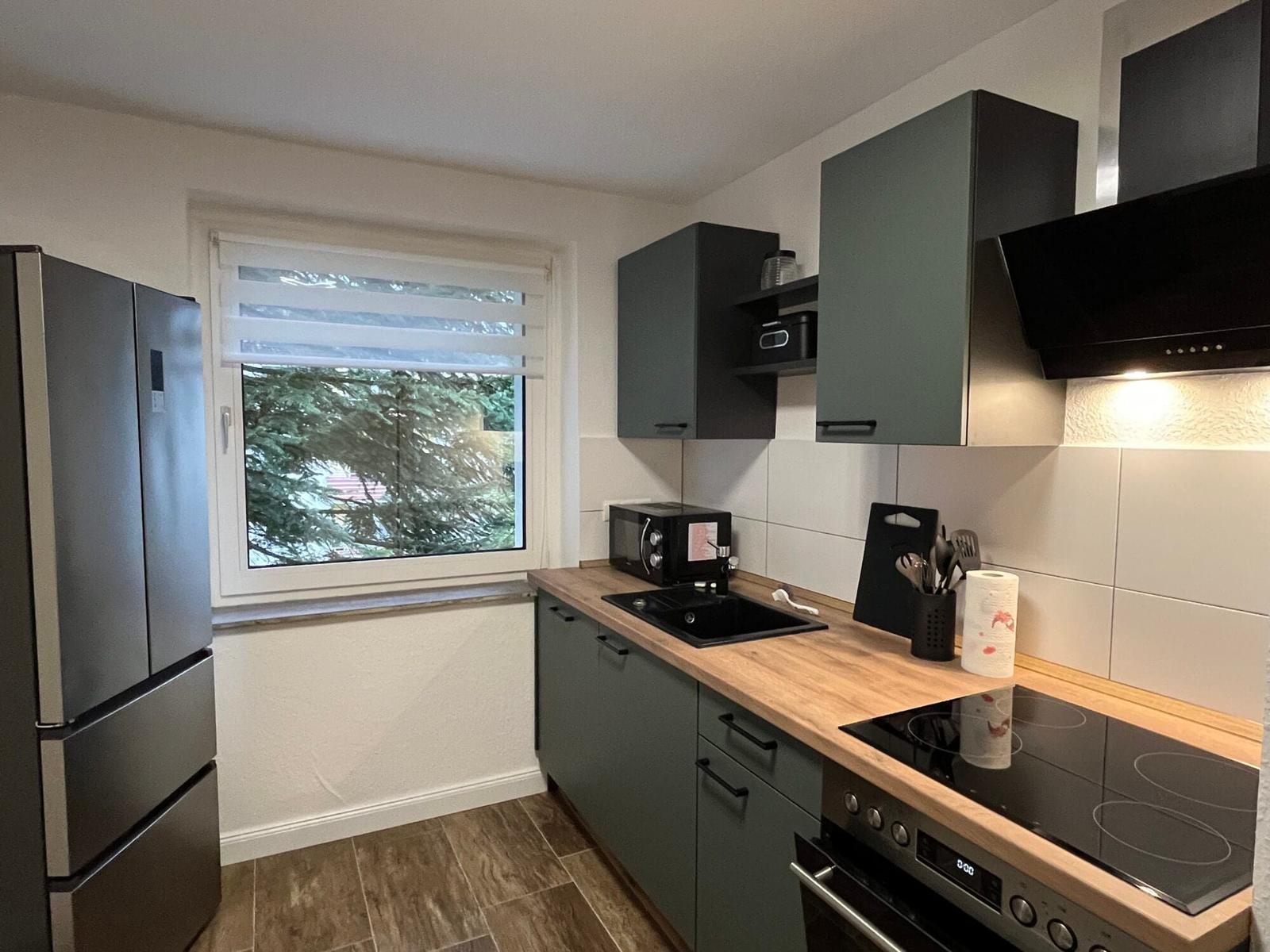 Küche mit dunklen Schränken, Holz Arbeitsplatte und Fenster mit Blick auf Bäume.