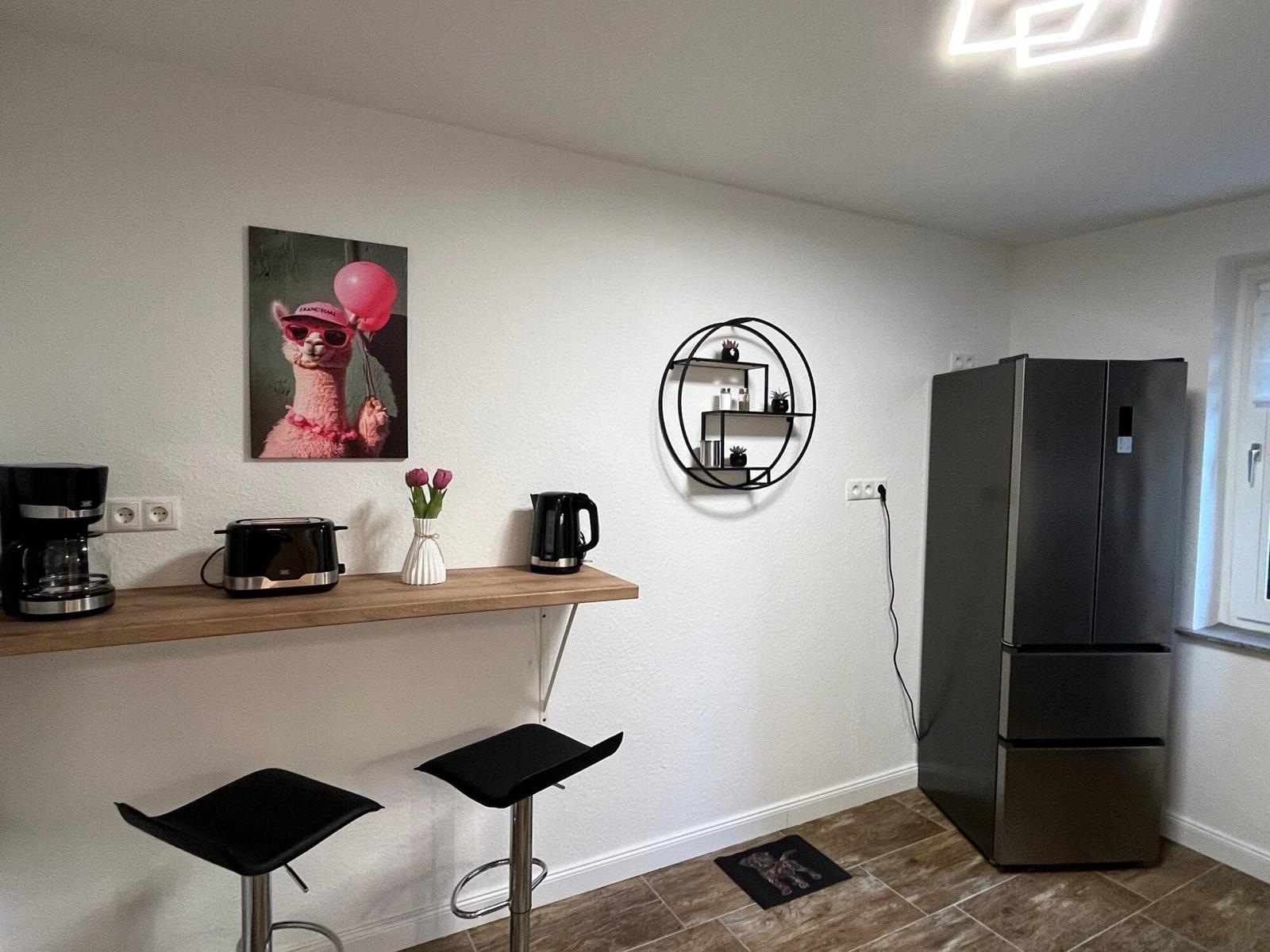 Küche mit Barhocker, Kühlschrank und Wandregal.