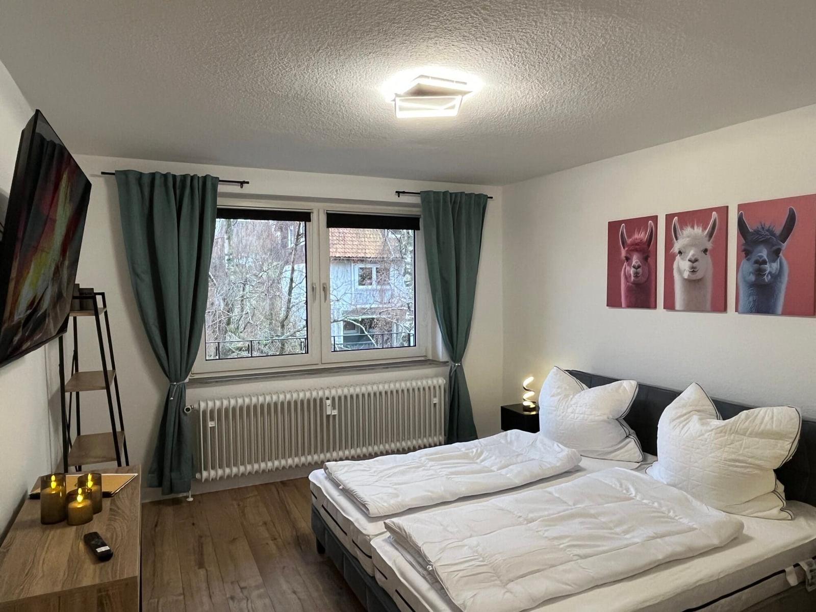 Schlafzimmer mit Doppelbett, Fenster, TV und Wandbildern von Lamas.