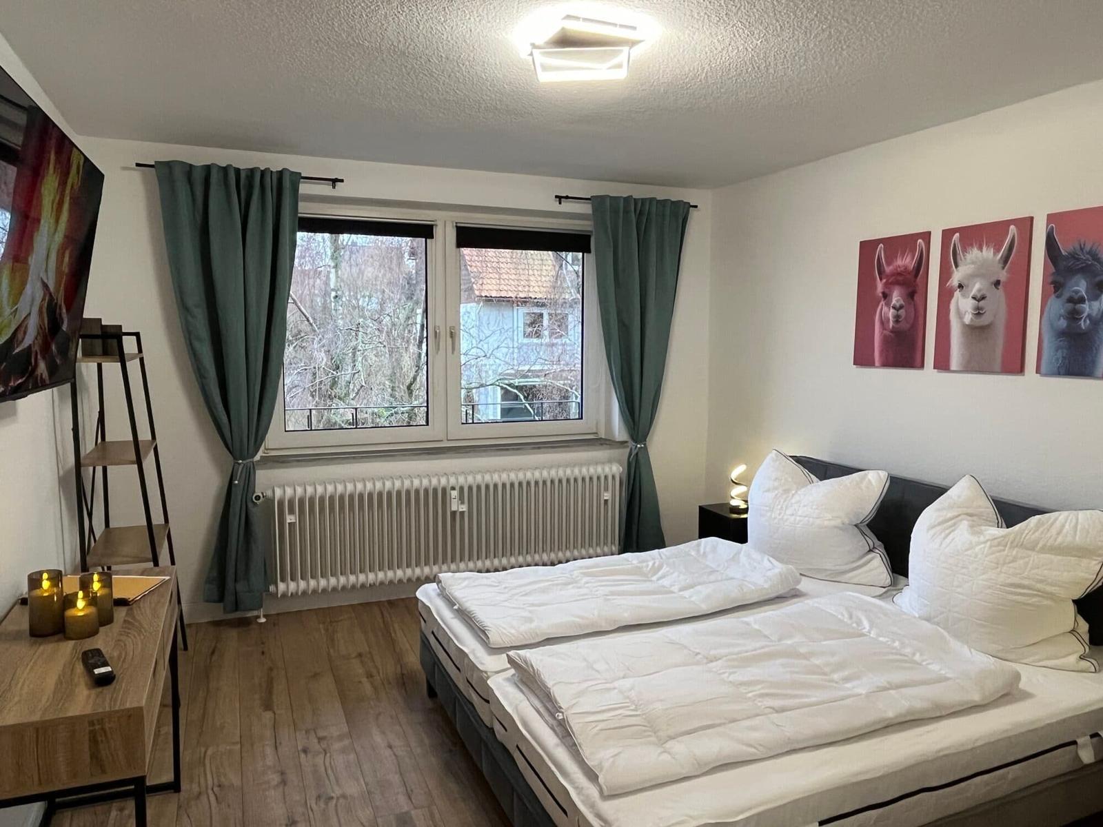 Schlafzimmer mit Doppelbett, Fenster, Vorhängen und Wandbildern von Lamas.